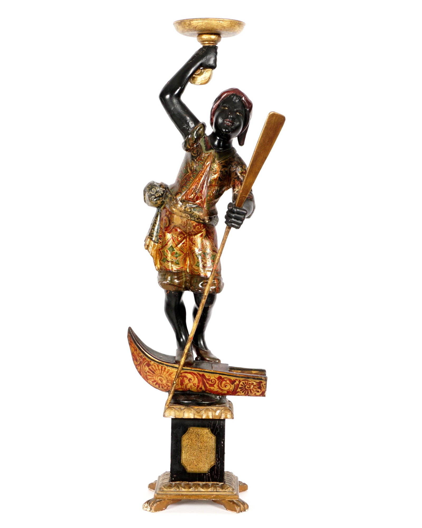 Venetian Carved Blackamoor Gondolier Figure: Polychrome paint decorated figure of a standing blackamoor gondolier standing on a partial gondola. Figure is holding a paddle in one hand, other arm raised holding a trumpet form candleholder. Eboniz