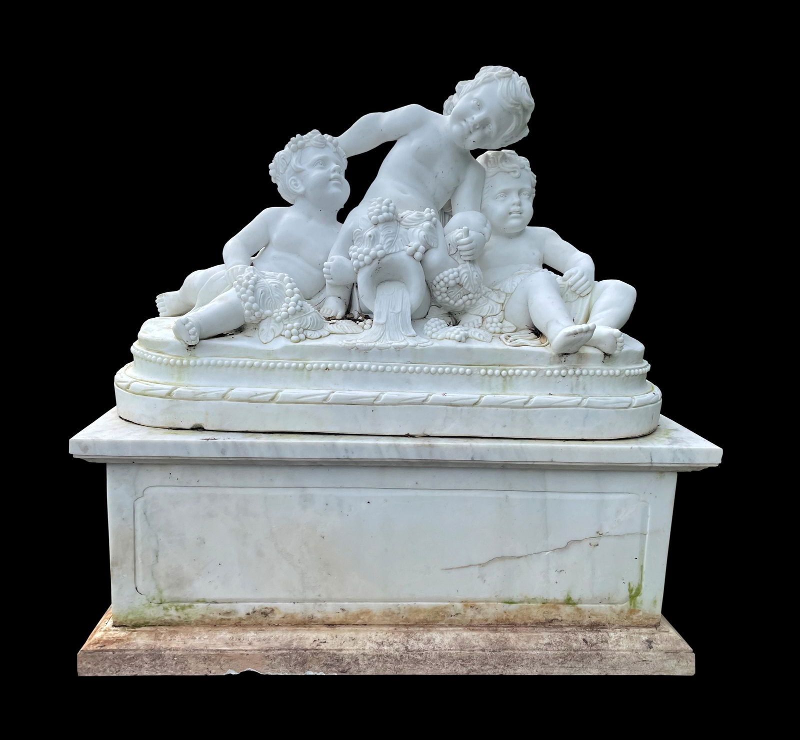 Palatial Neoclassical Carved Marble Sculpture: Carved marble garden sculpture, depiction of three bacchanalian putti on oval base, set upon a large rectangular marble plinth. No visible signature. Overall 51" h. x 51.25" x 23.75". Condition: Sever