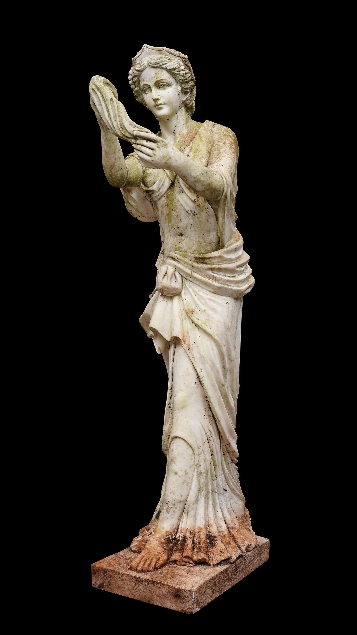 Marble Garden Sculpture of Neoclassical Woman: Figure of a standing neoclassical woman with crown and holding a scarf, no visible signature, overall approx. 71"h. x 20" x 28". Condition: Obvious signs of weathering. Shippers Note: Requires several