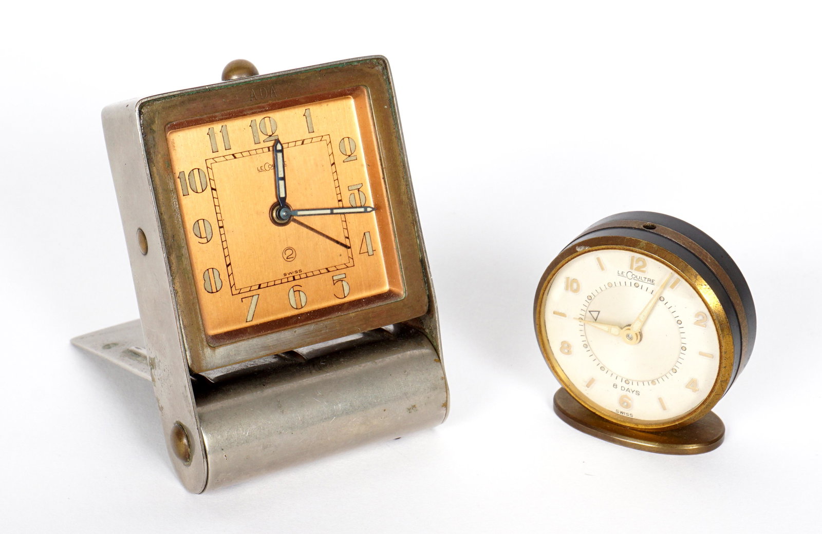 Two LeCoultre Travel Alarm Clocks: Two pieces total to include 1) Rectangular with folding steel cover, square copper dial, 3.25" x 2.25" x 1". Currently running. 2) Round clock on base, white dial, 1.75" dia. Currently not running.