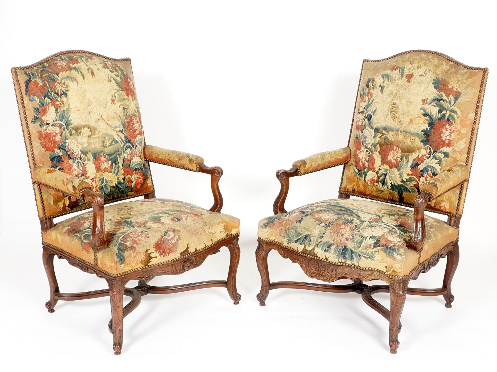 Pair 19th C. Louis XV Carved Fauteuil Arm Chairs: Walnut frames, carved and shaped handholds and supports, carved serpentine skirt, shaped legs ending in scroll feet. Tacked needlepoint upholstery with floral and animal motifs. Overall 43.5" h. x 29"