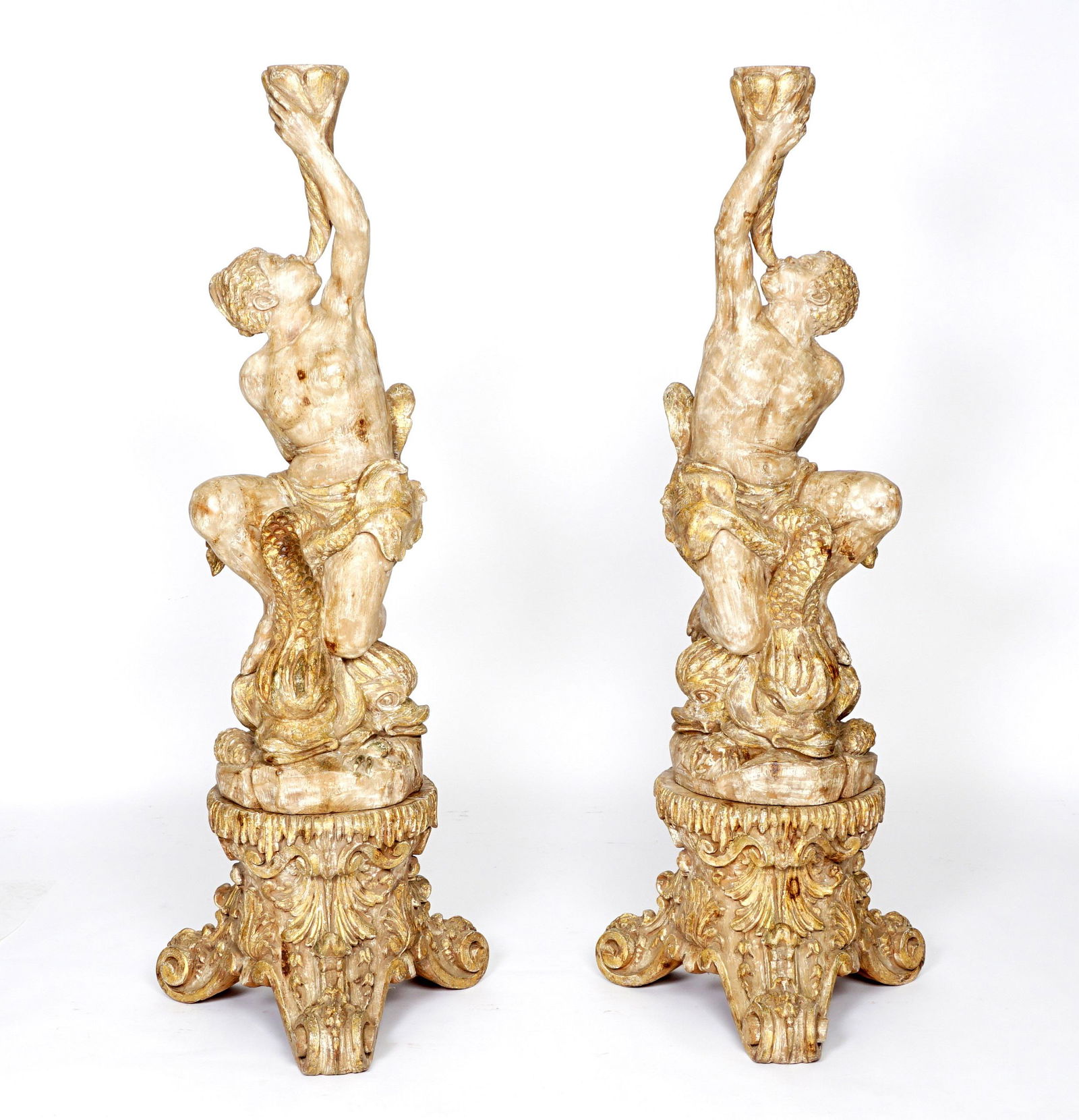 Pair Blackamoor Carved Floor Torchieres: Figural male and female blackamoor figures blowing shell horns, seated on stylized dolphins, foliate scroll bases on three splayed feet. Traces of white and gilt paint accents remain, overall 59" h. x