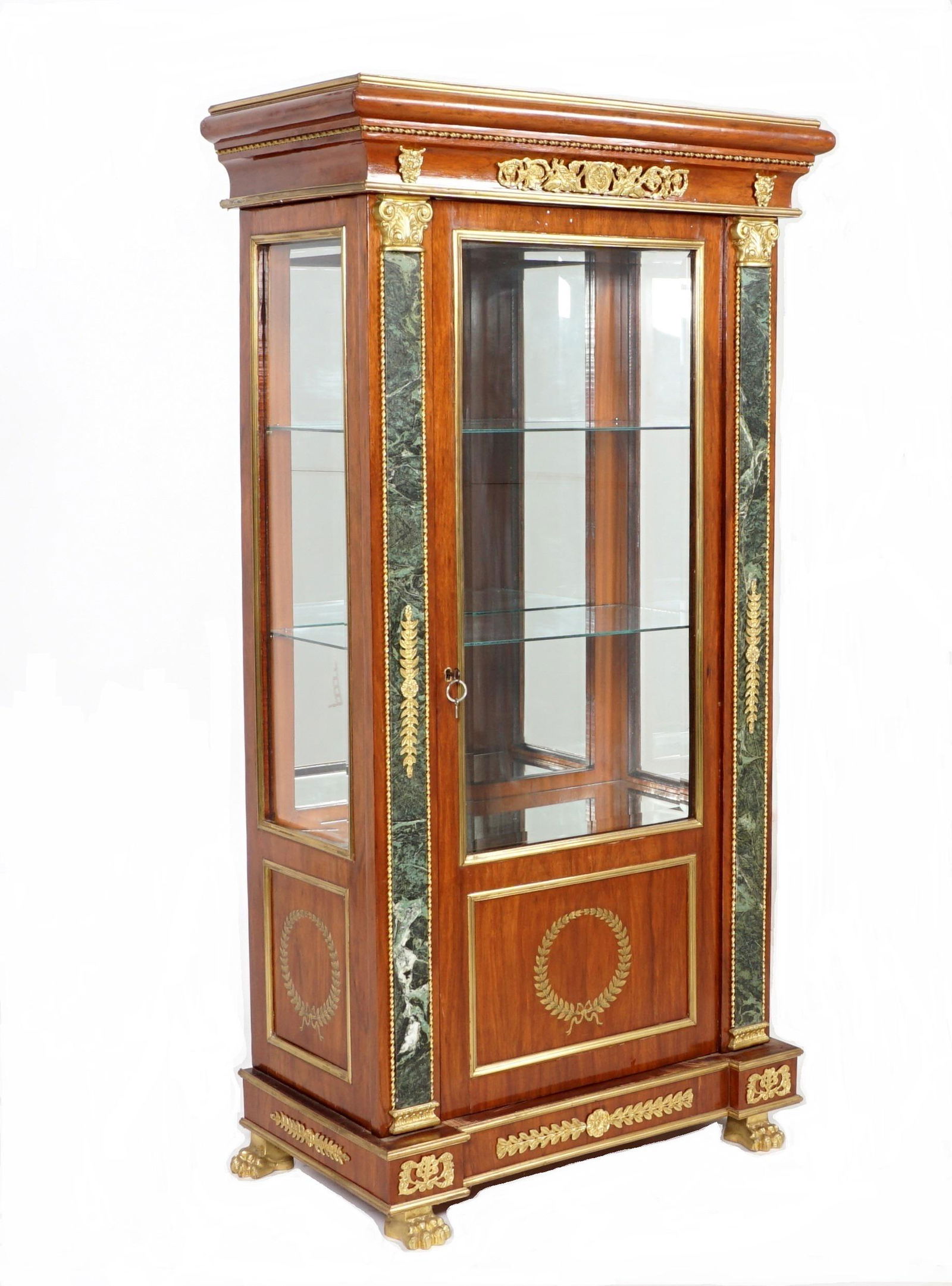 French Gilt Bronze Mounted Curio Cabinet: Bullnose cornice over gilt bronze decoration. Beveled glass door and sides, lower brass inlaid wreath motif panels. Marble stiles with gilt bronze accents. Mirror back interior, two glass shelves, all