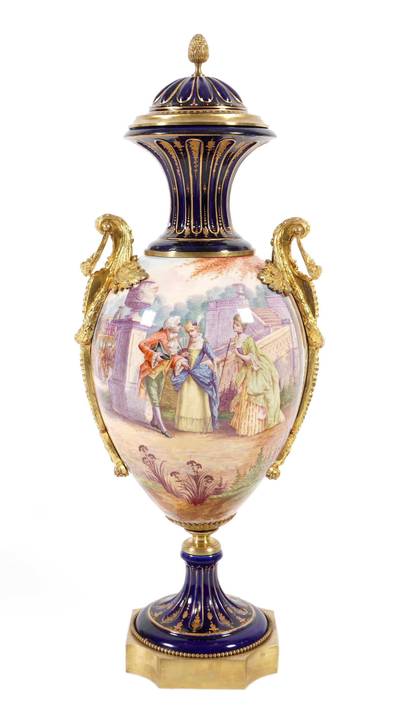 Large Sevres Style Gilt Metal Mounted Urn: Pineapple finial on removable lid, cobalt blue ground at top rim and foot, hand painted French courtyard genre scene on body, applied gilt metal handles. Marked under lid, overall measures 28.75" h. x