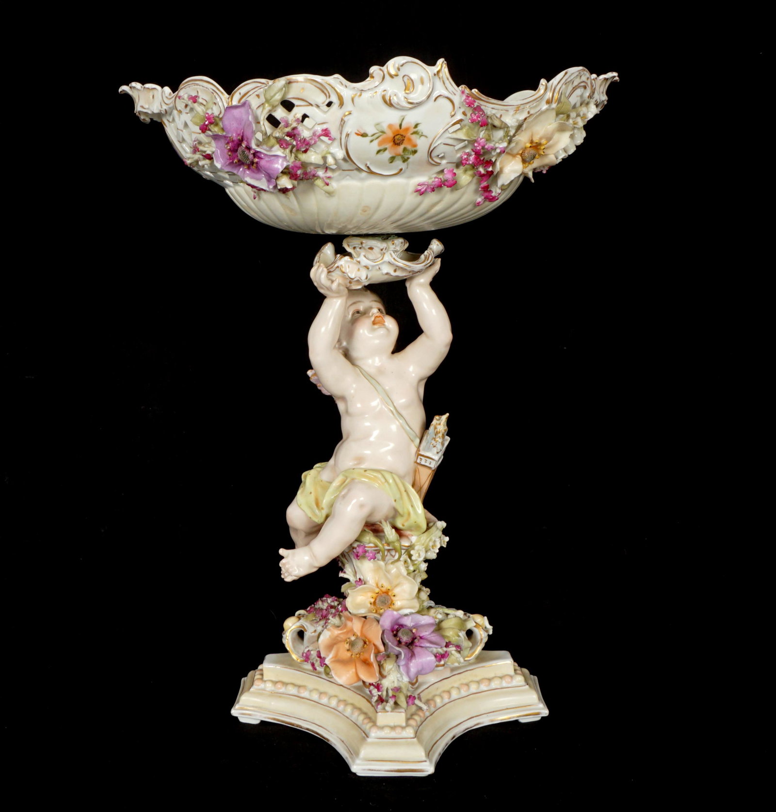 Large Schierholz Cherub Reticulated Centerpiece: Porcelain figural cherub sitting on a pedestal supporting a removable reticulated bowl, applied flowers. Marked under base, overall 19.25" h. x 14.5" x 12". Condition: Restoration to base, chips to fl