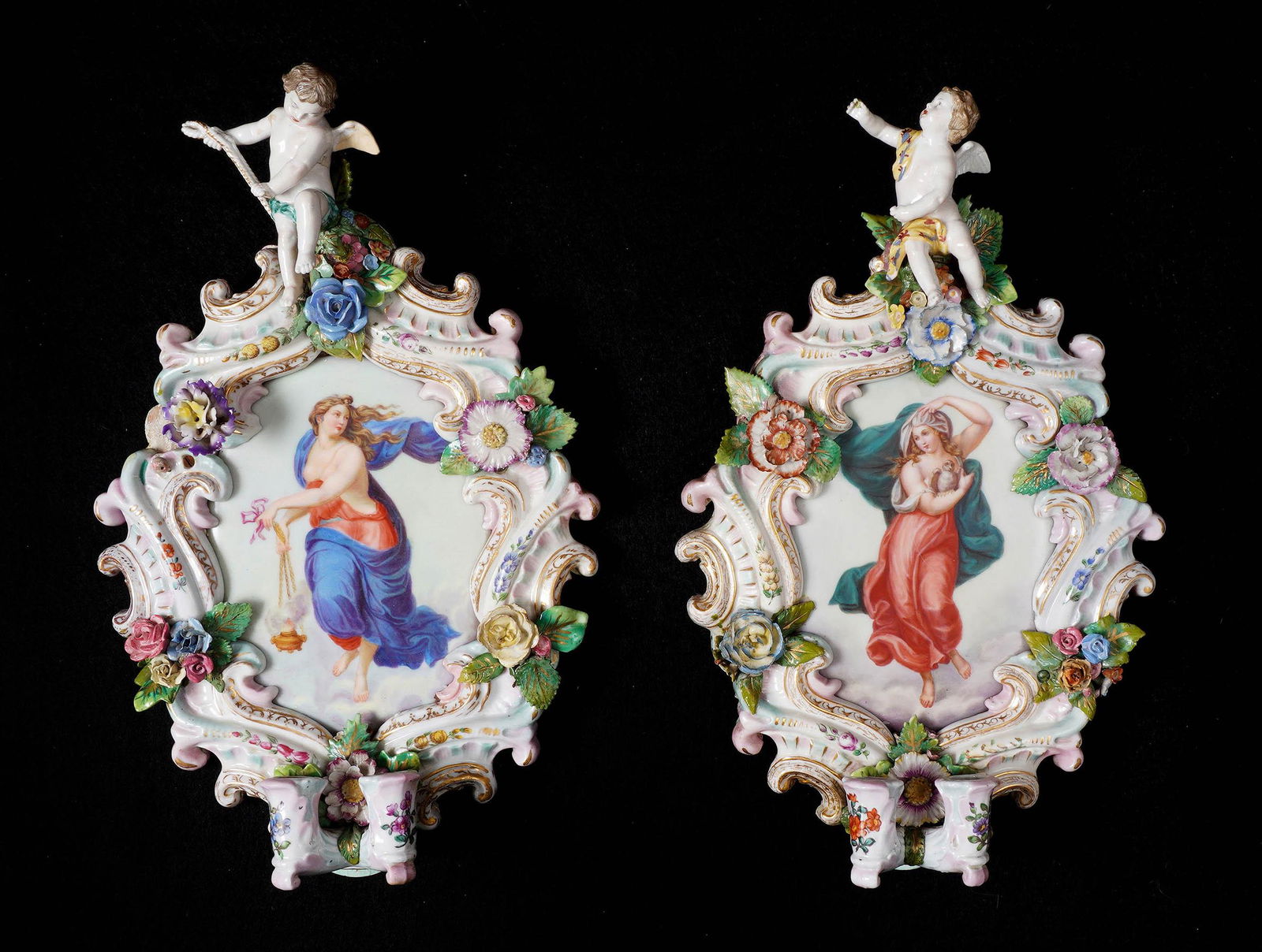 Pair Meissen Style Porcelain Wall Sconces: Each with center hand painted plaque with neoclassical maidens. Frames with figural cherub, applied flowers and foliate decoration, two candle holders. No visible markings, overall 14.5" x 9" x 2.5".