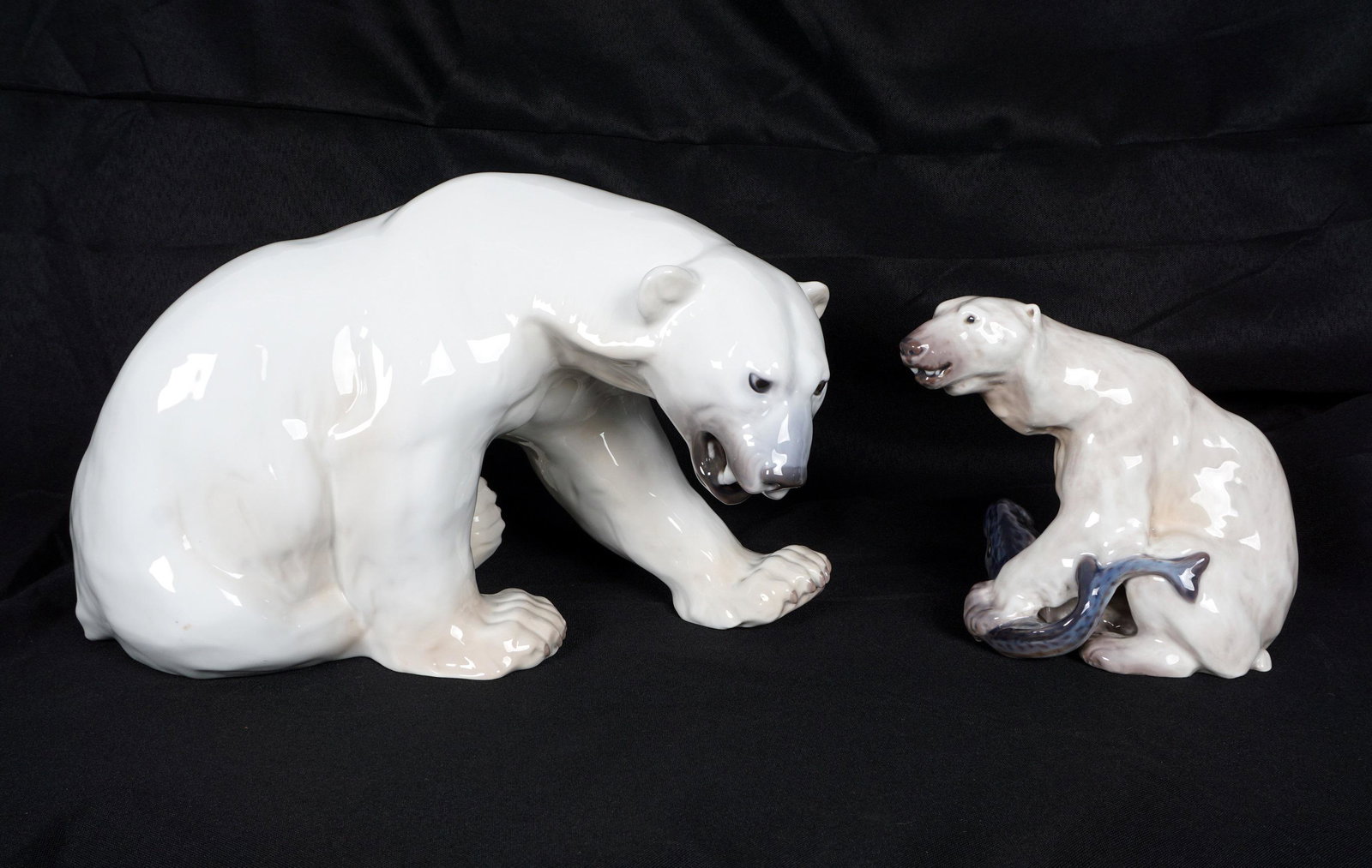 Pair Danish Porcelain Polar Bears B & G and DJ: Two pieces total to include 1) Large Bing and Grondahl seated bear with mouth open, #1857, 8" h. x 13.5" x .5". 2) Dahl Jensen polar bear with fish, #1272, 6" h. x 6.5" x 4". From the estate of a prom