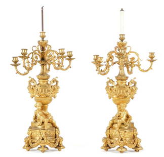 Pair French Gilt Bronze Figural Candelabra: Pair gilt bronze candelabra, each with six foliate scroll arms, electrified center fixture, urn form center support over figural putti, one reading and the other holding a painting of a tree. Base