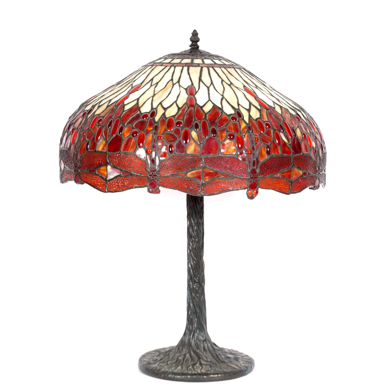 Tiffany Style Dragonfly Jeweled Leaded Glass Lamp: Red jeweled dragonfly motif leaded glass shade, tree trunk form bronze base, triple socket fixture. Base measures 31" x 11", shade 11.5" x 24". Condition: Cracks on two red "jewels", some dragon heads