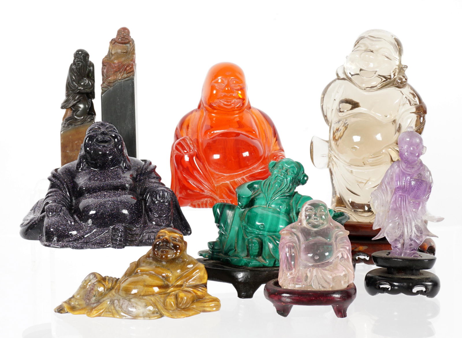 Nine Piece Collection of Figural Buddhas: An assembled collection of nine Buddhas in varying position. To include smoky quartz, amber, tiger eye, malachite, amethyst quartz, soapstone seals, purple composite. Tallest standing quartz measures