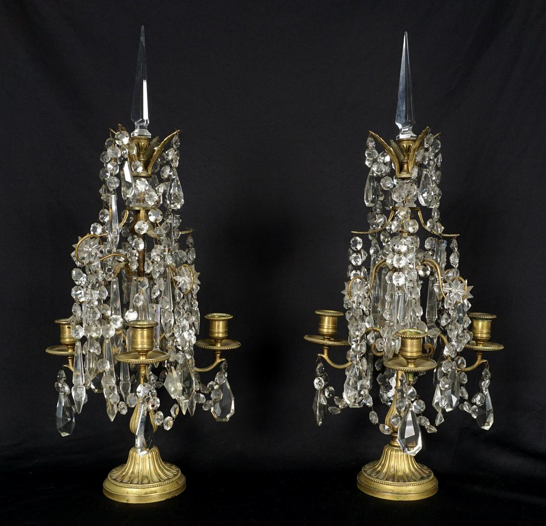 Pair Gilt Bronze and Crystal Table Chandeliers: Gilt bronze bases with scroll arms, four candle bobeche, crystal prism drops, swags, and spire. Overall 25.5" h. x 11.5". Condition: Spotting to bronze, the occasional chip or missing prism may be dis