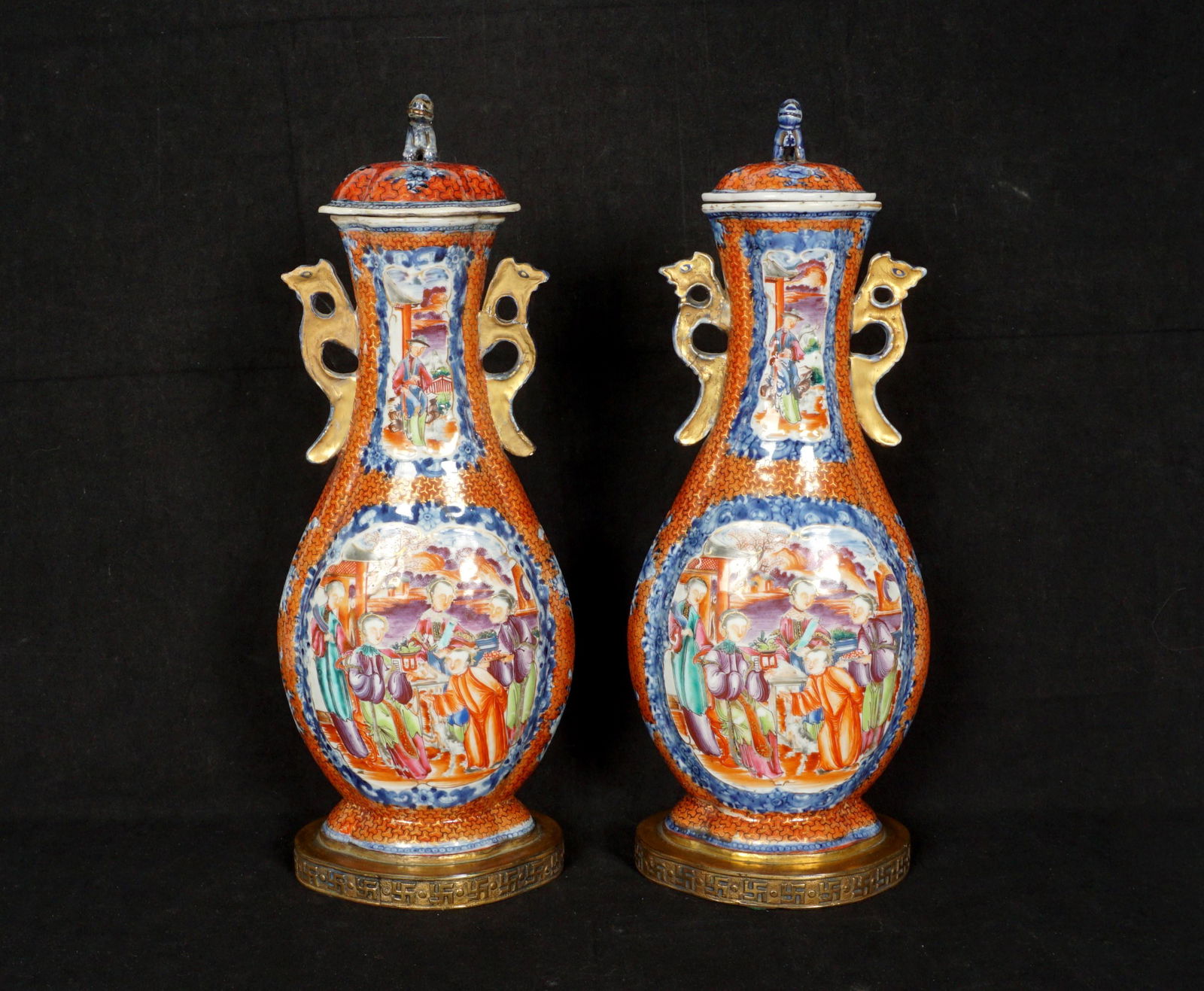 Pair Chinese Rose Mandarin Covered Vases: Lids with applied foo dog finials, matching rose mandarin genre scenes in reserves, applied handles, affixed to embossed brass bases, overall 14" h. x 5" x 4". Condition: Repair to one handle. From th