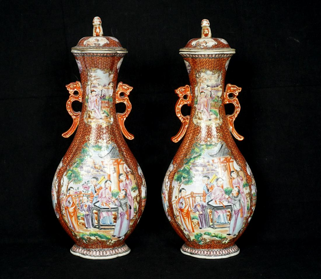 Pair Chinese Rose Mandarin Covered Vases: Lids with applied foo dog finials, matching rose mandarin genre scenes in reserves, applied handles, overall 14" h. x 6" x 3.75". Condition: One with significant repair to neck and cover. From the est