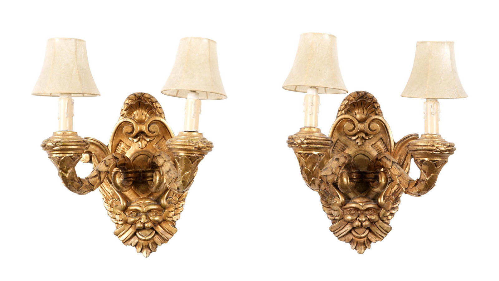 Pair French Carved Giltwood Sconces: Pair turn of the century carved giltwood sconces, scroll and foliate motif over winged masks backplate. Two scroll arms, electrified, no visible markings. Overall 13.75" h. x 12.75" x 9.5". Sold with