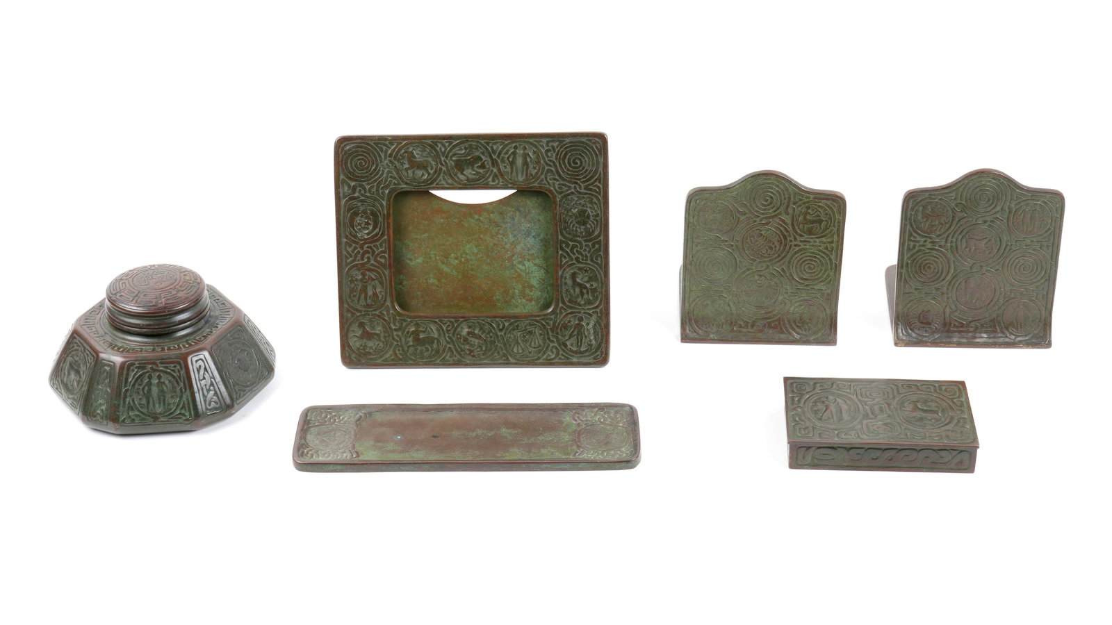 Tiffany Studios Bronze Zodiac Desk Set: Seven pieces total in the patinated bronze Zodiac pattern by Tiffany Studios New York, to include 1) Large inkwell 1072, glass insert, 3.5" h. x 6.5". Chips to insert. 2) Hinged box 810, 1.25" h. x 5.