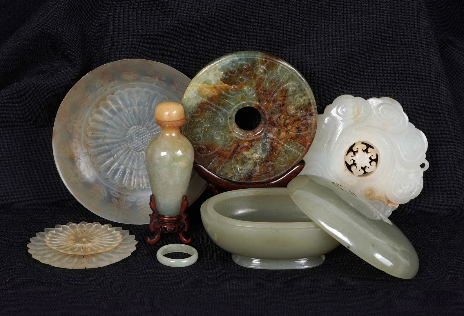 Seven Piece Collection of Carved Jade Items: Seven pieces jade or similar stone total to include 1) Floriform medallion, reticulated center spins, 2.5" dia. 2) Mottled nephrite bi disc with stand, 2.75" dia. 3) Translucent small dish, 3.25" dia.