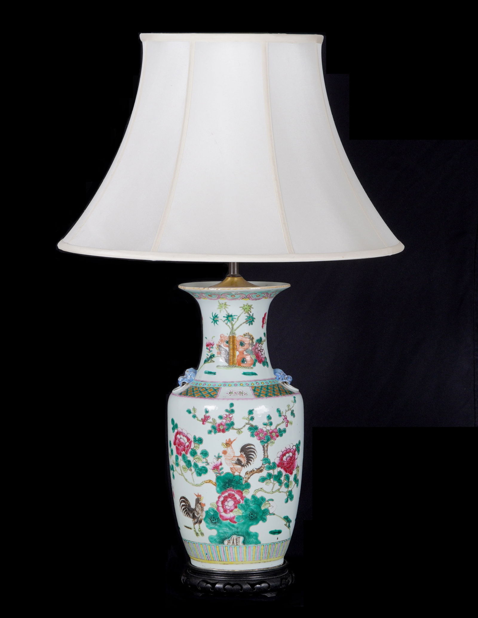 Chinese Famille Rose Vase Mounted as a Lamp: Baluster form Famille Rose decorated vase with flowering branches and roosters, applied dog head "handles". Carved wood base, 23" h. excluding harp, 8". Sold with cloth shade 13.75" h. x 21.25".