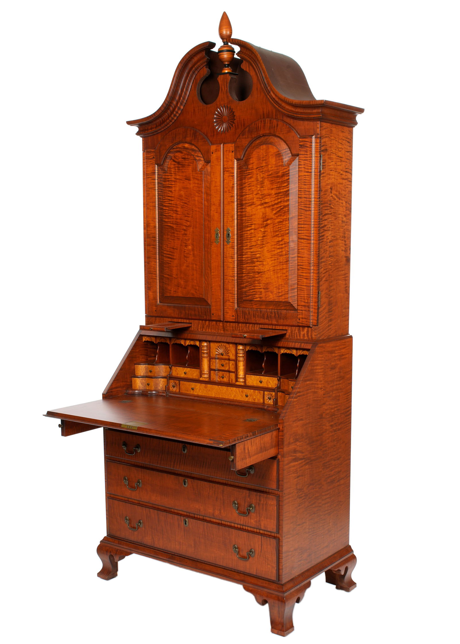 Eldred Wheeler Bonnet Top Secretary Bookcase: Bench made tiger maple case, broken arch bonnet top, center turned spire finial, crest with carved medallion. Two arched blind doors open to fitted interior with shelves and pigeon holes. Lower case w