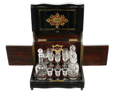 Antique French Inlaid Ebonized Tantalus Box: Lift top ebonized case. Brass, fruitwood, and abalone inlaid medallions of top and front. Fitted interior with three assembled decanters with stoppers, 11 assorted cordial glasses. All on four ball fe