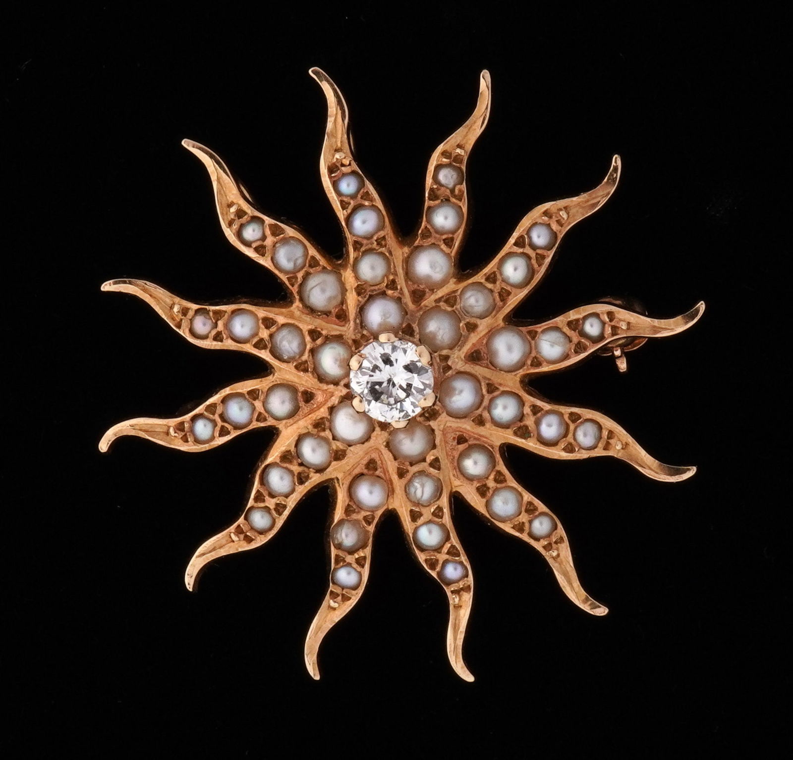 14k Gold Diamond and Seed Pearl Sunburst Brooch: 14k yellow gold sunburst design brooch, prong set approx. .25ct center diamond, inset seed pearls on each arm. 1.5" dia. Approx. 5 grams inclusive. Note: Several pearls with cracks.