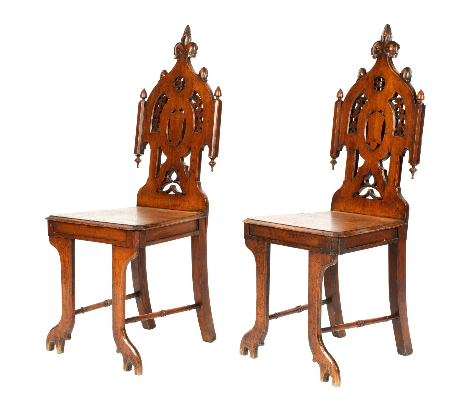 Pair Walnut English Gothic Revival Hall Chairs: Gothic revival reticulated carved backs, trapezoidal wood seats, shaped legs. Overall 42" h. x 17" x 19". Condition: Chips, dings, and losses.