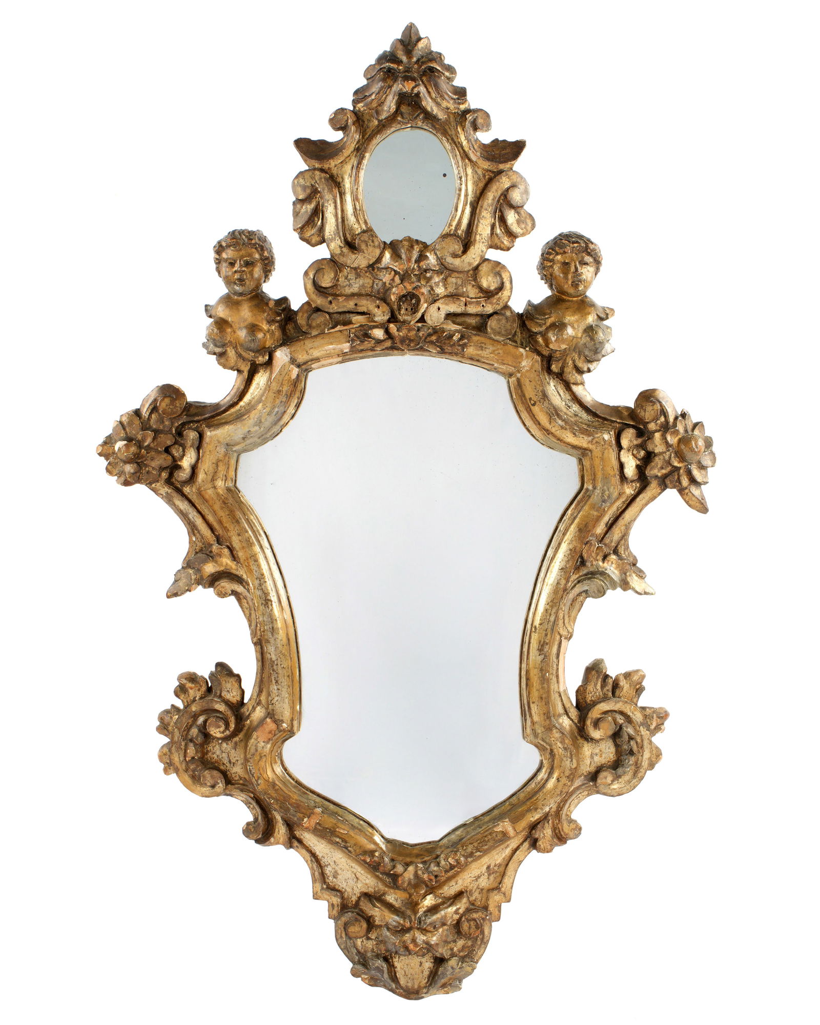 Early Italian Rococo Carved Giltwood Mirror: Crest with mask above oval mirror, above center mask. Figural bust of putti either side. Serpentine frame with floral and foliate scroll motifs, conforming mirror, lower mask finial. Overall 42" h. x