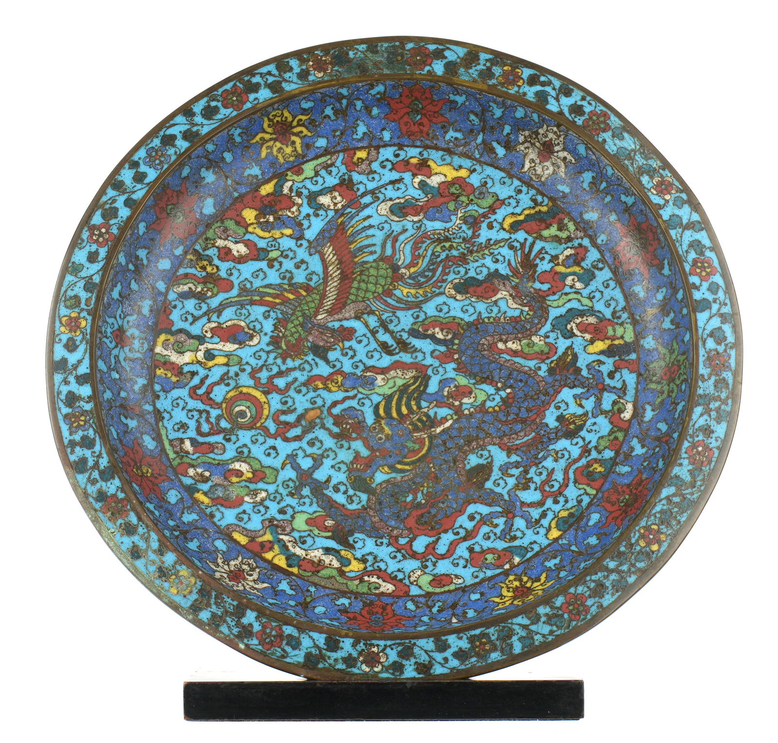Antique Chinese Dragon Phoenix Cloisonne Charger: Ming or Qing cloisonne charger, blue ground, decorated with four toed dragon, phoenix, flaming pearls, smoke and foliate motifs. Unmarked, overall 2.75" h. x 16.5". Sold with wood stand, 13.5" h. x 9"