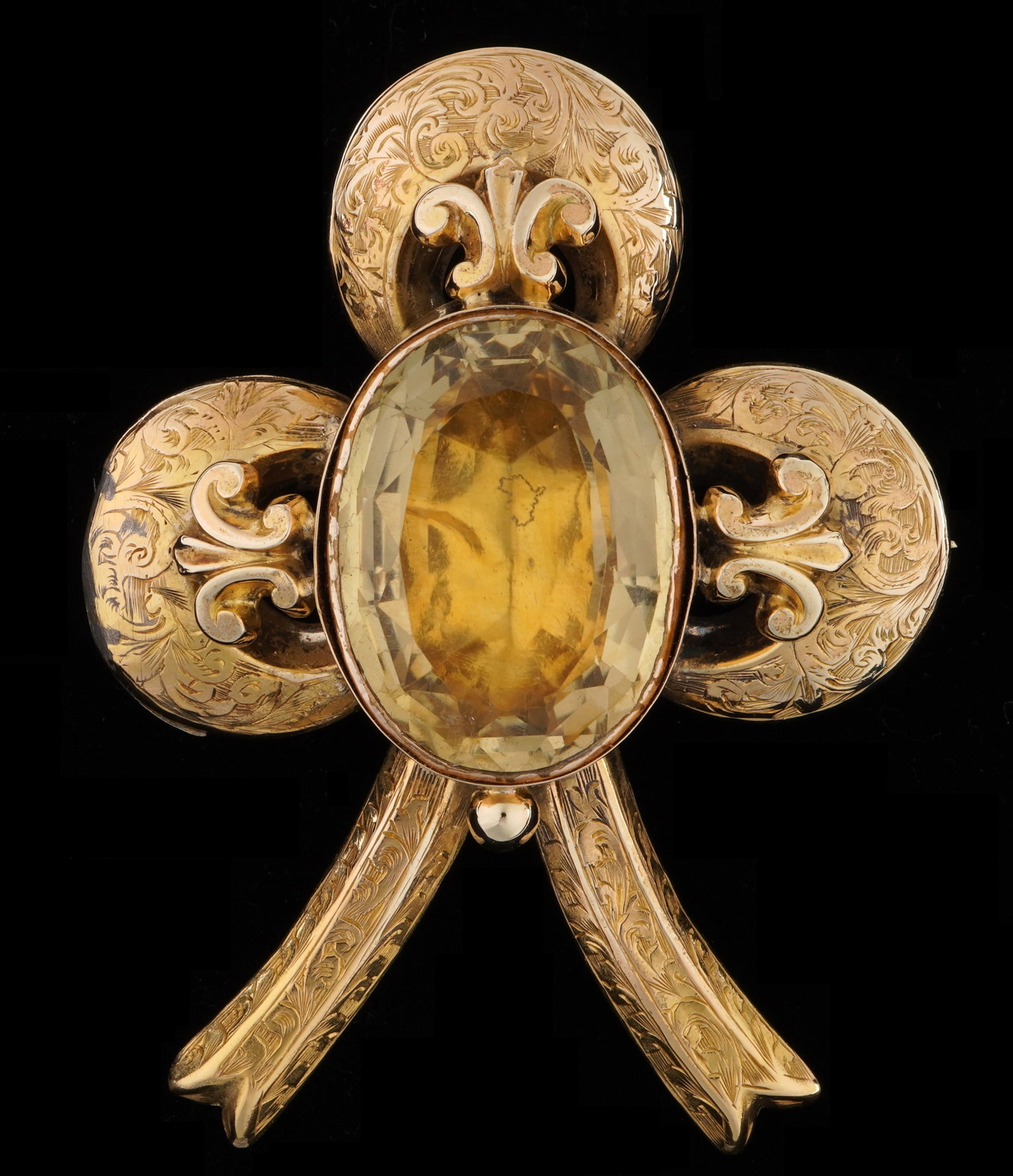 Victorian 14k Gold & Citrine Cloverleaf Brooch: 14k yellow gold framed, center oval cut citrine approx. 25mm x 20mm, three fleur die lis bezel guards, hand engraved flora decoration. Verso with oval window, 2.5" h. x 2", approx. 18 grams inclusive.
