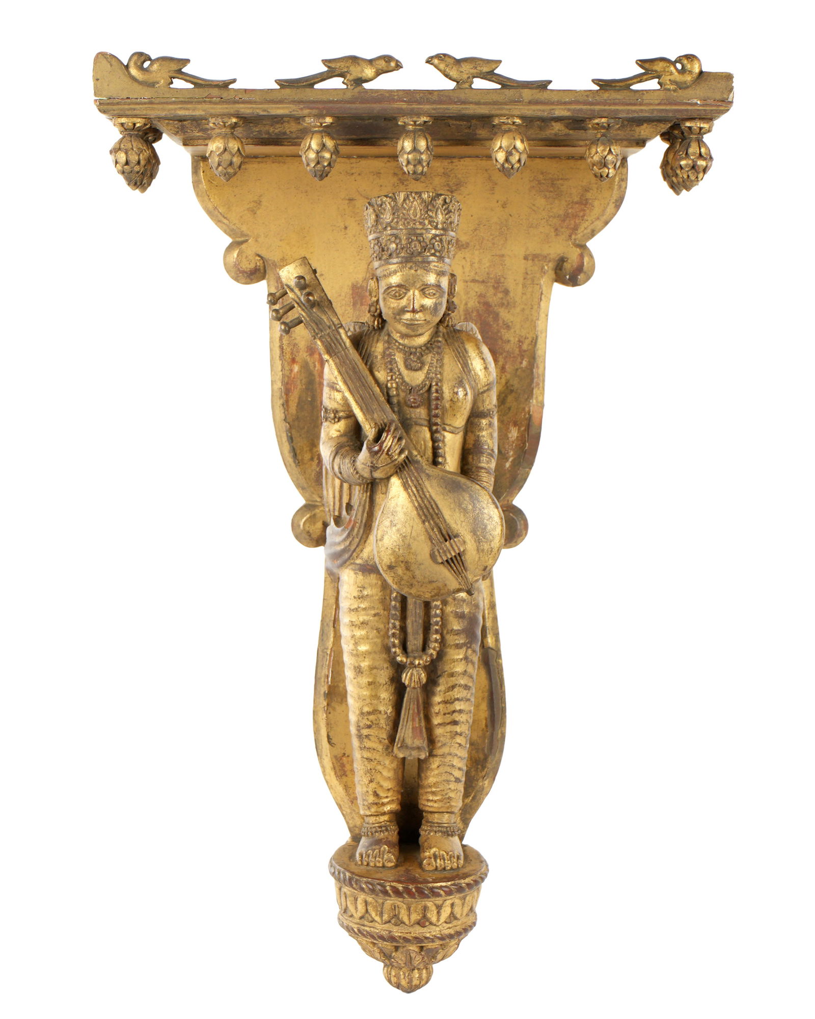 Carved Gilt Wood Saraswati Figural Wall Shelf: Carved gilt wood wall shelf or bracket, top with figural birds over figural depiction of the Hindu goddess Saraswati with wings playing a veena. Overall 18.25" h. x 11" x 5.75". Condition: Wear to gil