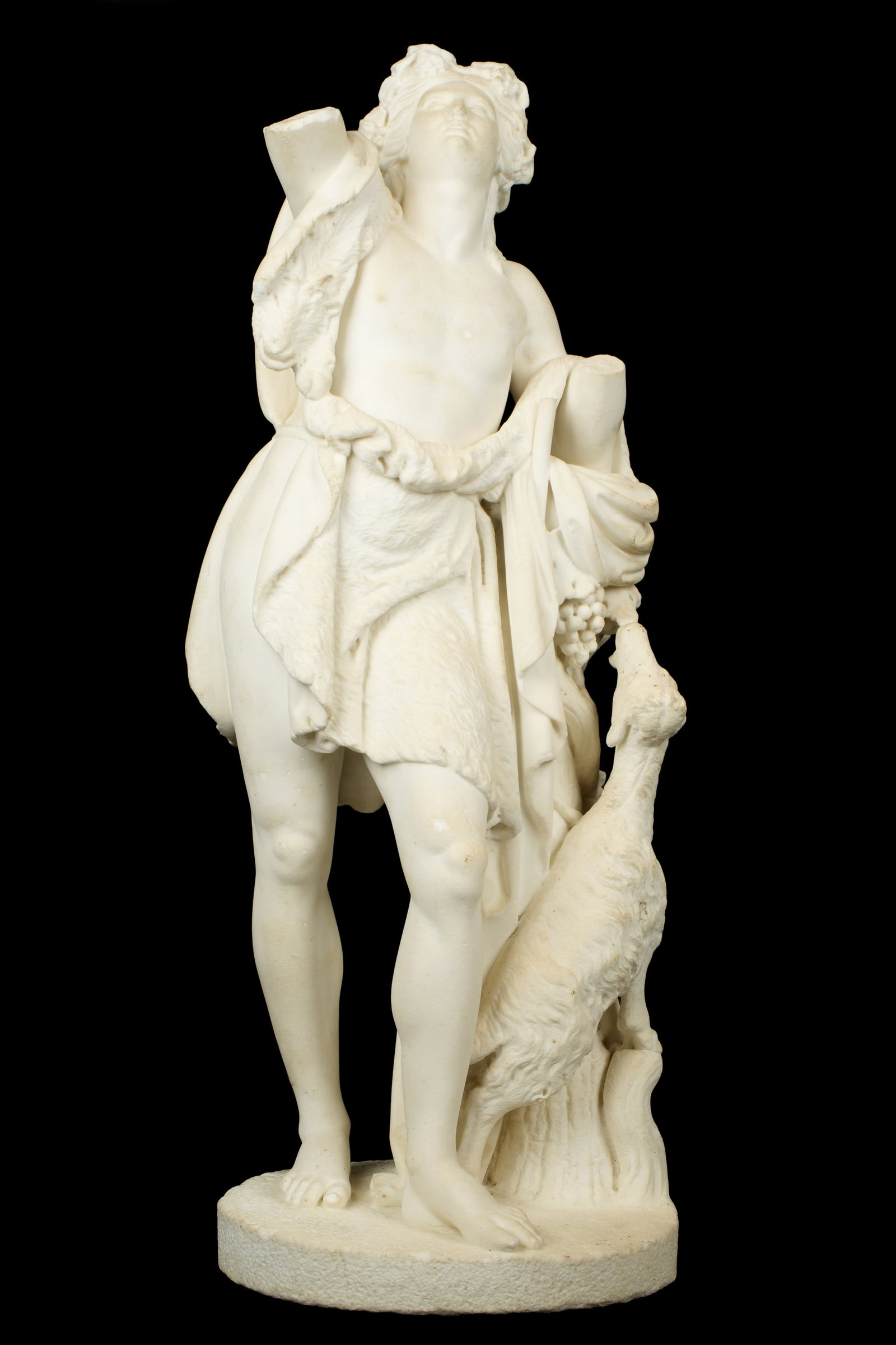 Carved Marble Bacchus with Goat Sculpture: Depiction of Bacchus in flowing garb with goat chewing on grape vine, no visible signature. Overall 30.5" h. x 11.5" x 8". Condition: Missing arms, chips, repairs to base.