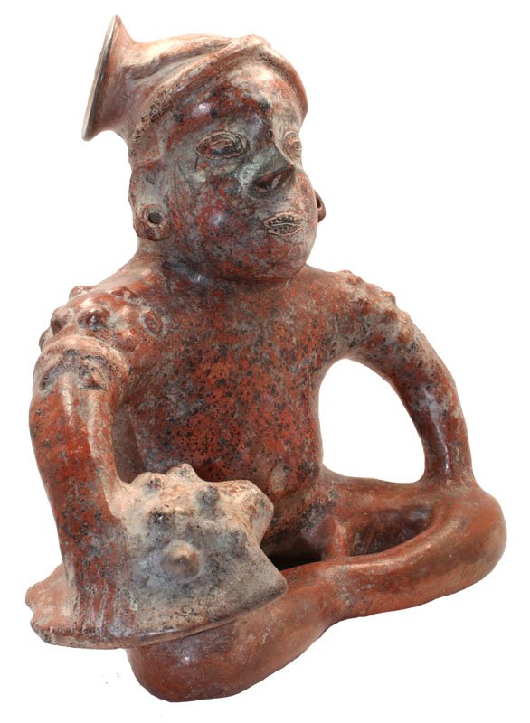 11" H. Well modeled redware Tropmetero. Seated male: 11" H. Well modeled redware Tropmetero. Seated male figure with incised turban, node applique shoulders, with arms on knees. He holds a conch shell trumpet in his right hand. Colima. MX. 250 BC to 250