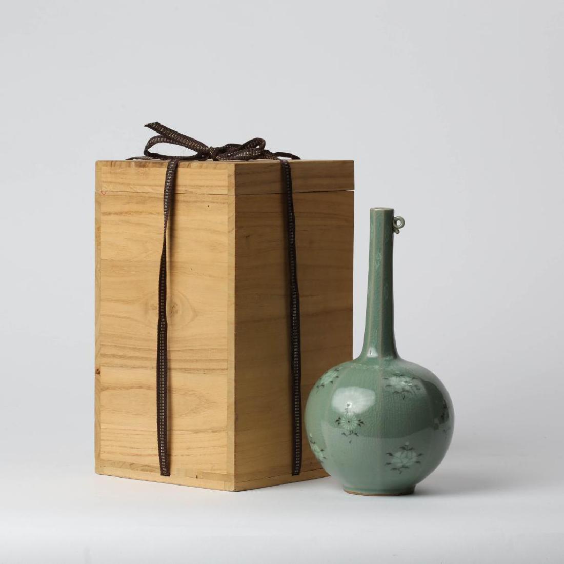 A KOREAN INLAID CELADON STICKNECK VASE AND CASE: Fine celadon stickneck vase with inlaid florals, small loop near top of the fluted neck. Signed base. Stands 1.5 inches. Includes the original wooden case with woven cloth ties.Box measures 12.75 x 7.