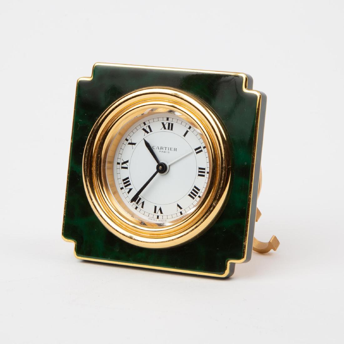 CARTIER ENAMELED TRAVEL DESK CLOCK: A Cartier gilt brass travel clock, manual wind, with green tortoiseshell-effect lacquered case, hinged stand, and Roman numeral hour markers on a white dial.Â Marked Cartier Paris on dial. Back of c