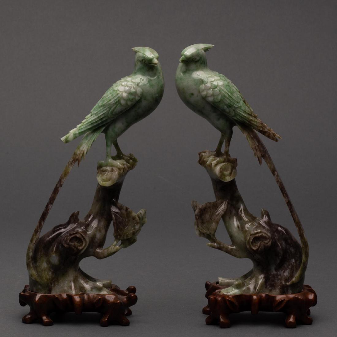PAIR OF CARVED CHINESE SAUSSURITE BIRDS, 20TH CENTURY: Green and russet saussurite carving of ribbon-tailed birds resting on tree branches, with stands. Nicely carved with attention to the birdsâ€™ feathers and gnarled tree trunks. In Chinese, the wo