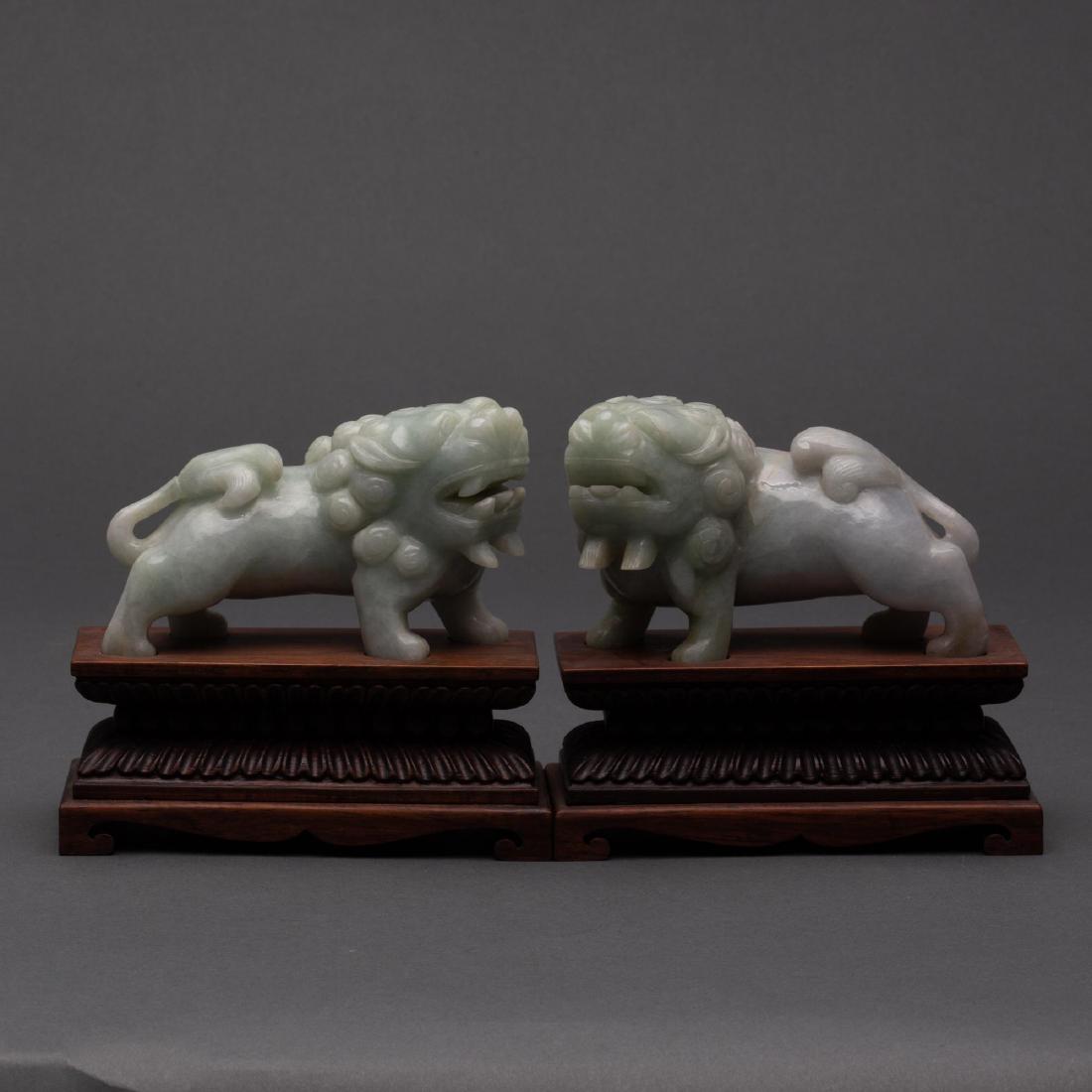 CARVED CHINESE PALE-GREEN JADEITE JADE FOO DOGS, 20TH: Pair of carved pale-green jadeite foo dogs, or Buddhist lions, on wooden stands. They are considered guardians and can often be found in front of temples and residence. Each measures 2 3/4 x 4 3/4 inc