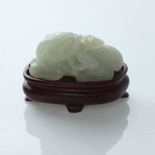 CHINESE NEPHRITE JADE CARVING OF AN AUSPICIOUS ANIMAL ,: Carved Nephrite of a recumbent mythical beast with its legs tucked under the body and head turned back, holding the fungus of immortality in its mouth, with stand. The fungus conveys the wish, “