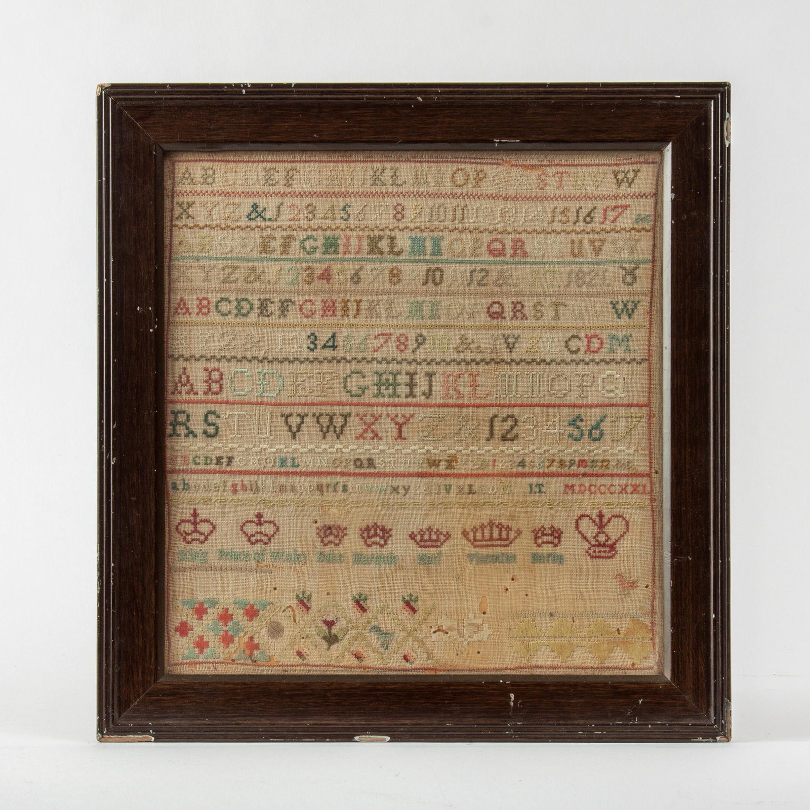 1821 Alphabet and Crown Sampler, with Inscription: A deftly executed 1821 alphabet sampler, with a row of labeled crown symbols of English royalty. The reverse of the original antique frame bears a hand-written inscription: "Grandmother June Tyley Whi