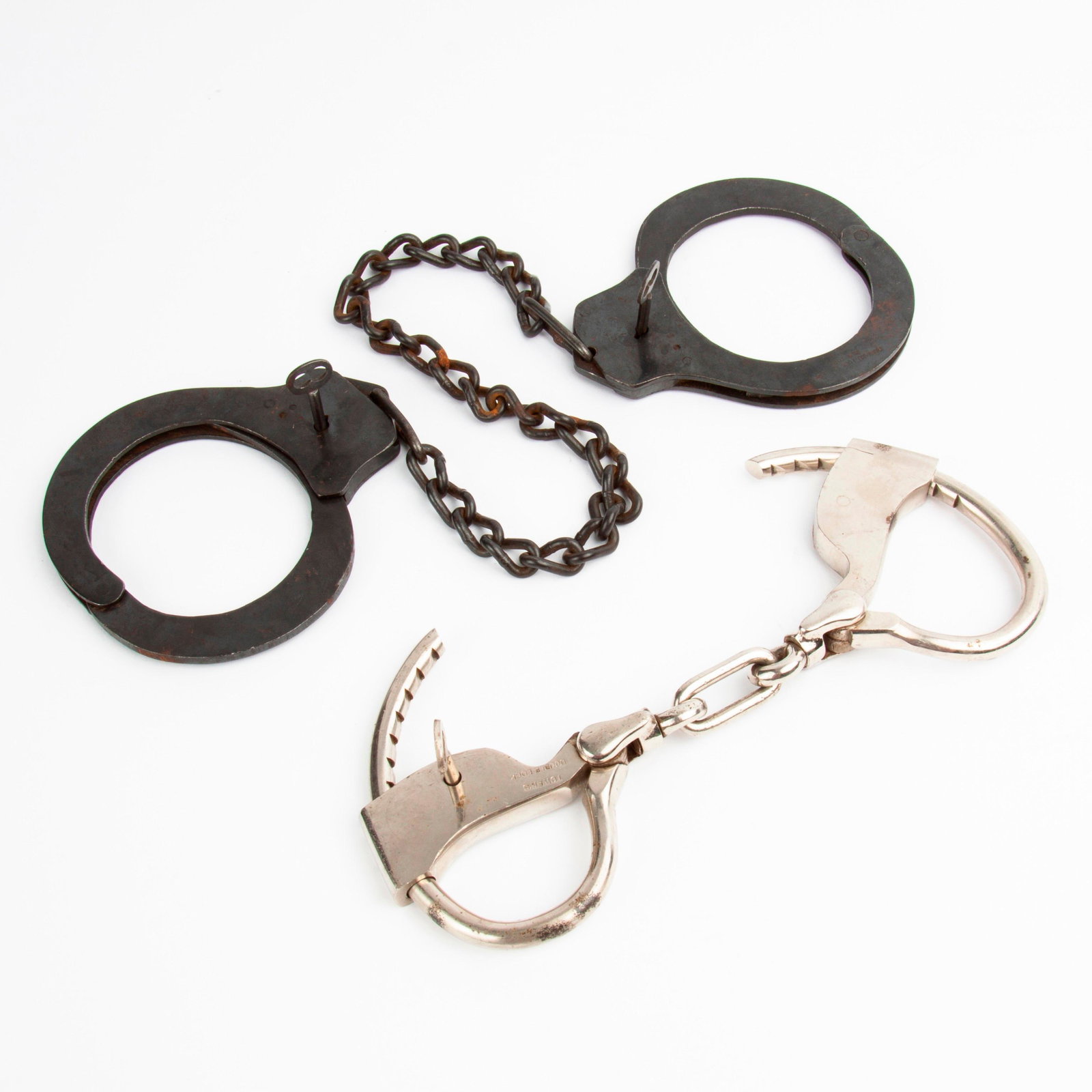 19th/20th c. Handcuffs and Leg Irons: A pair of handcuffs (late 19th c.) and a pair of leg irons (ca. 1930s). Each pair is fully functional, and offered with original keys. The steel handcuffs are marked "TOWER'S DOUBLE LOCK". The le
