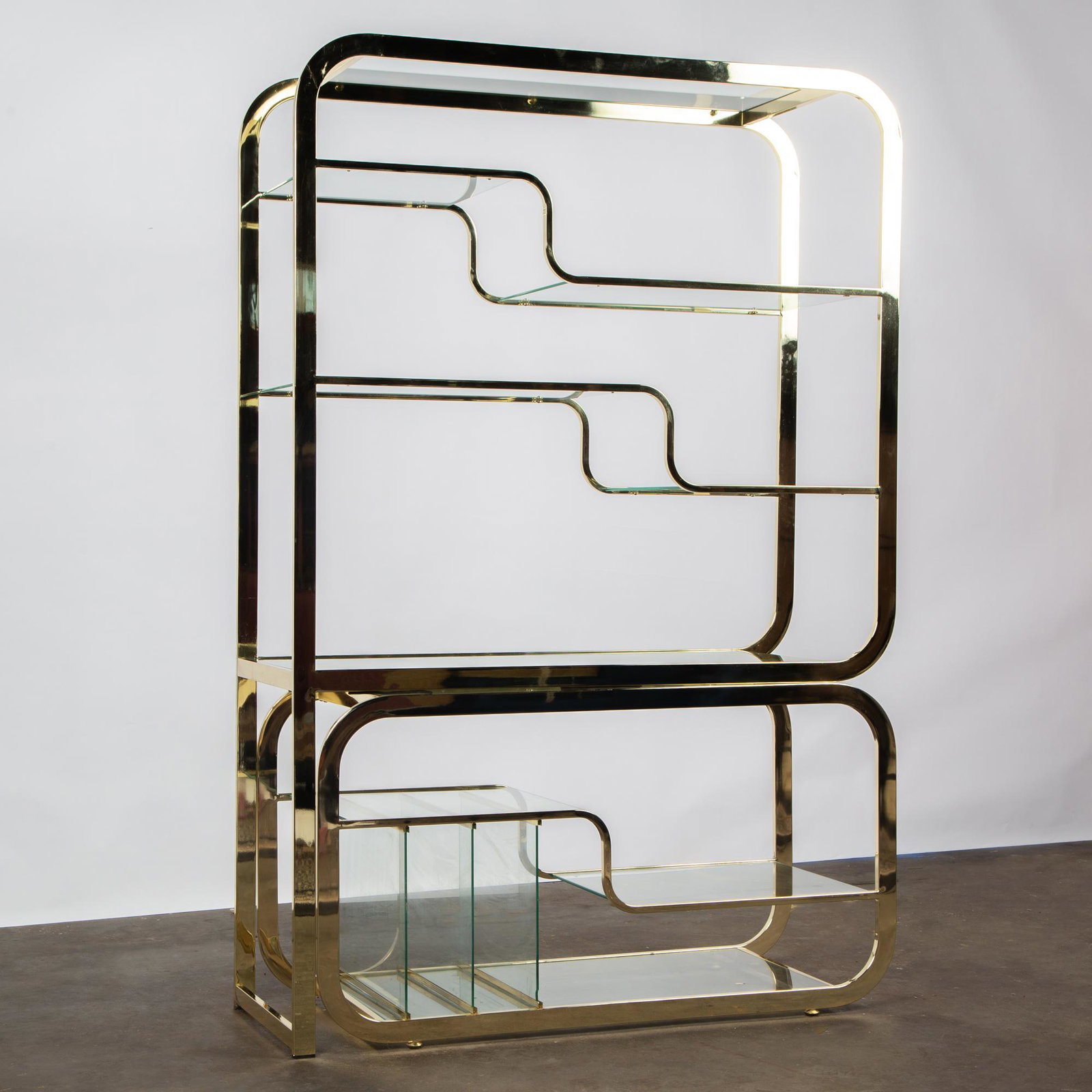 Milo Baughman for DIA: Adjustable Brass Etagere: A two-piece brass etagere with glass shelves, designed by Milo Baughman for the Design Institute of America, circa 1970. The bottom shelf is adjustable, sliding to the side. Unmarked. Measures 71