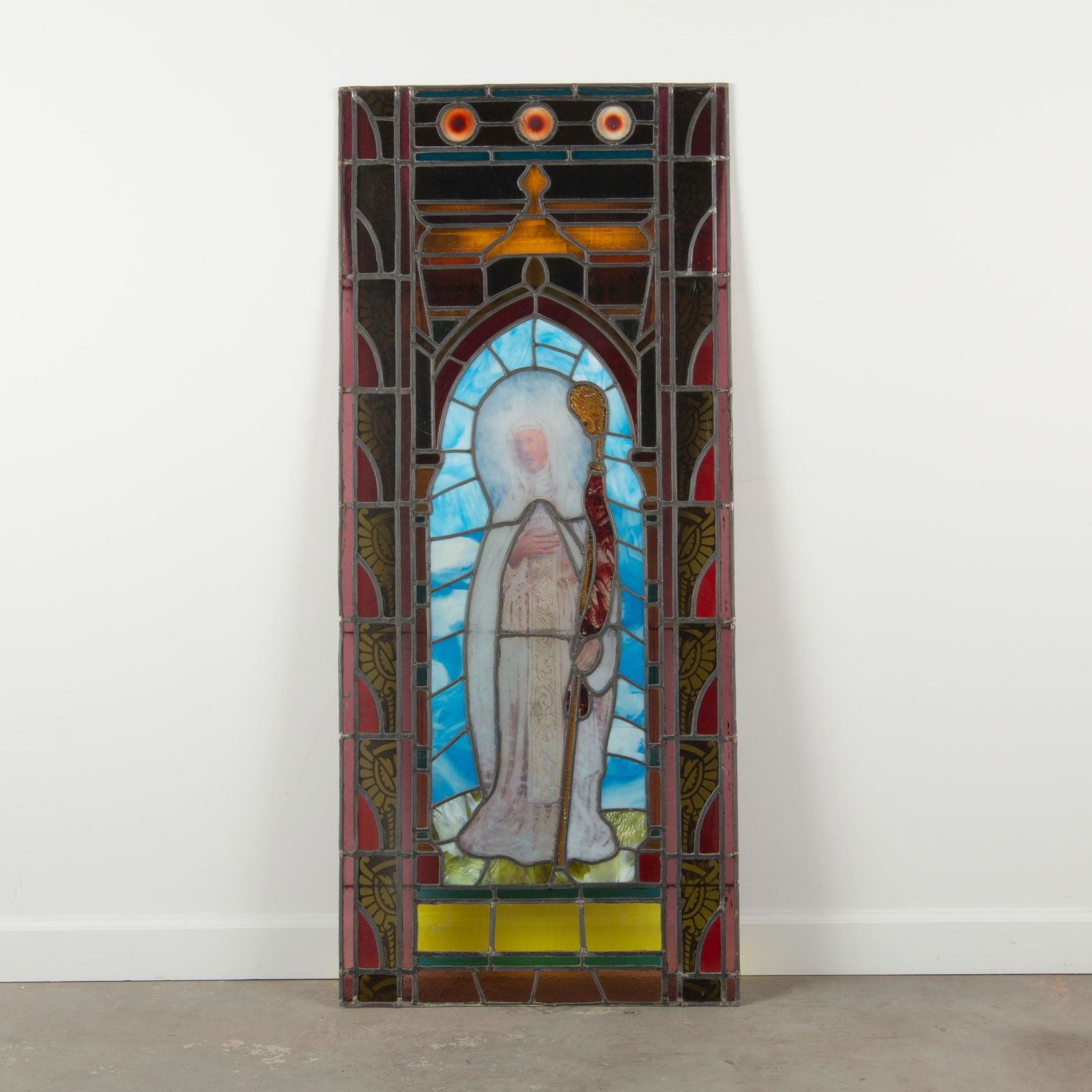 Stained & Leaded Glass, Late 19th c.: A late 19th c. stained and leaded glass panel depicting a saintly figure in a white robe, holding a staff, and standing in a gothic archway. Measures 61" x 26 1/4". From a private collection Kansas Ci