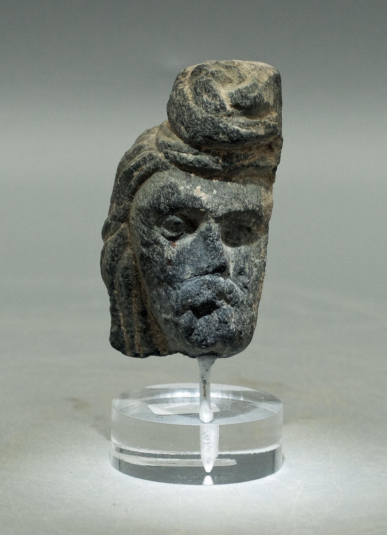 Gandharan Stone Head - Indus Valley, 3rd-4th C. AD: An excellent Gandharan stone head from the Indus Valley, ca. 3rd - 4th Century AD. This choice example is 2-1/4" high, is carved from the typical gray schist and depicts a bearded man adorned with a s