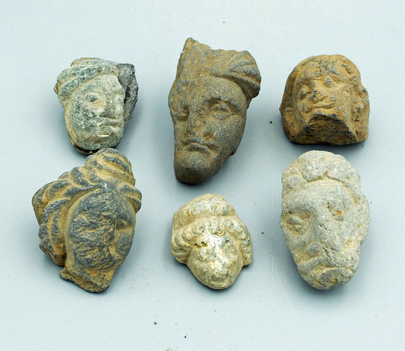 (6) Gandharan Stone Heads - Indus Valley, 4th C AD: A collection of six Gandharan stone heads from the Indus Valley, ca. 3rd - 4th Century AD. They are 1-1/8 to 1-5/8 inches high and are carved from the blue-gray schist characteristic of the region. Ea