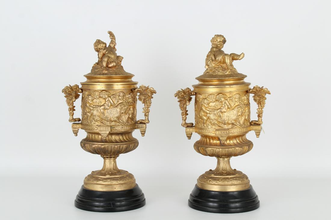 French Gilt Bronze Twin Handled Cherubic Urns: French Gilt Bronze Twin Handled Cherubic Urns. Depicting the scenes of the infant bacchus throughout exterior. Grape form handles. Height: 15 in.