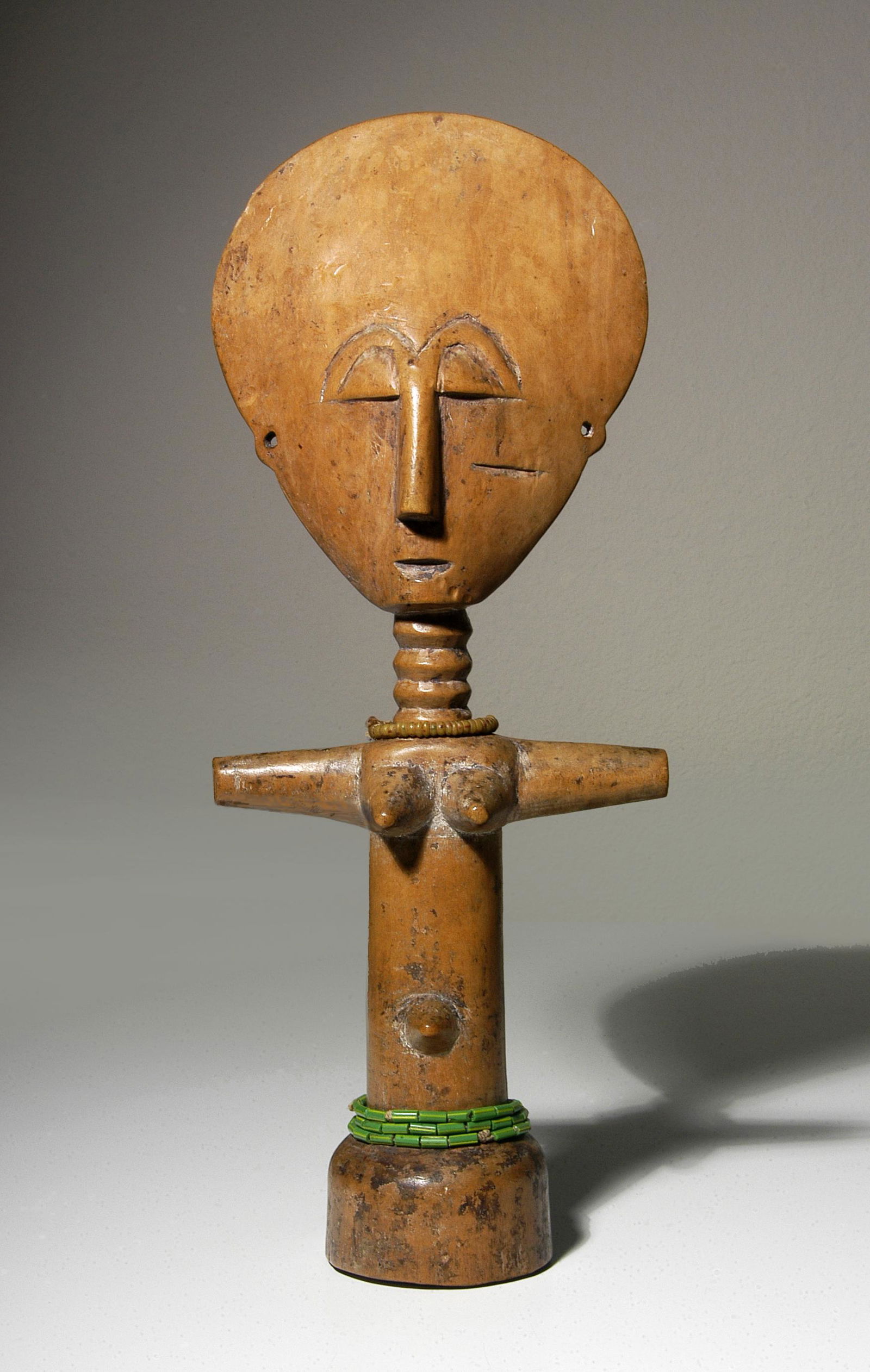 Bono/Akan Ppl Aku'aba Doll: Aku'aba doll 700 peoples Ghana Early-mid 20th century Wood with honey-brown, golden, aged patina; glass beads 14" x 5.5" Very fine condition with traces of kaolin pigment