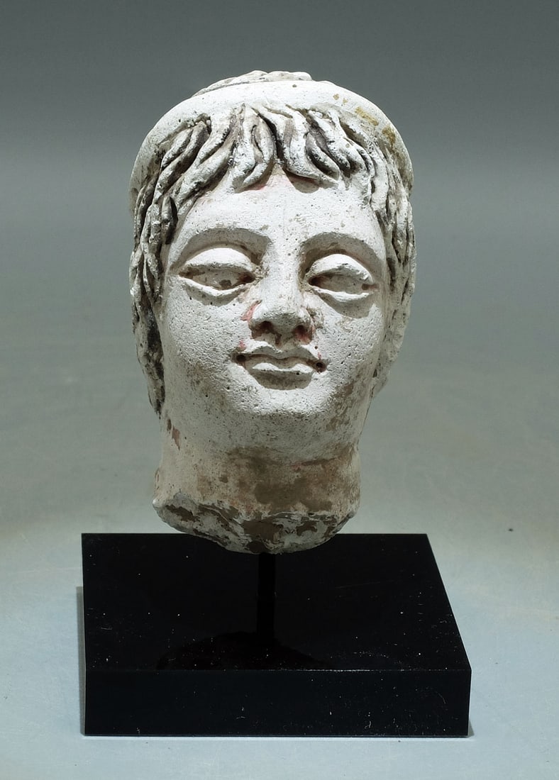 Gandharan Stucco Head - Indus Valley: A choice Gandharan stucco head from the Indus Valley, ca. 4th - 5th Century AD. This lovely example is 3-1/4 in. high and portrays a beautiful youth with black hair. The expressive face is delicately 