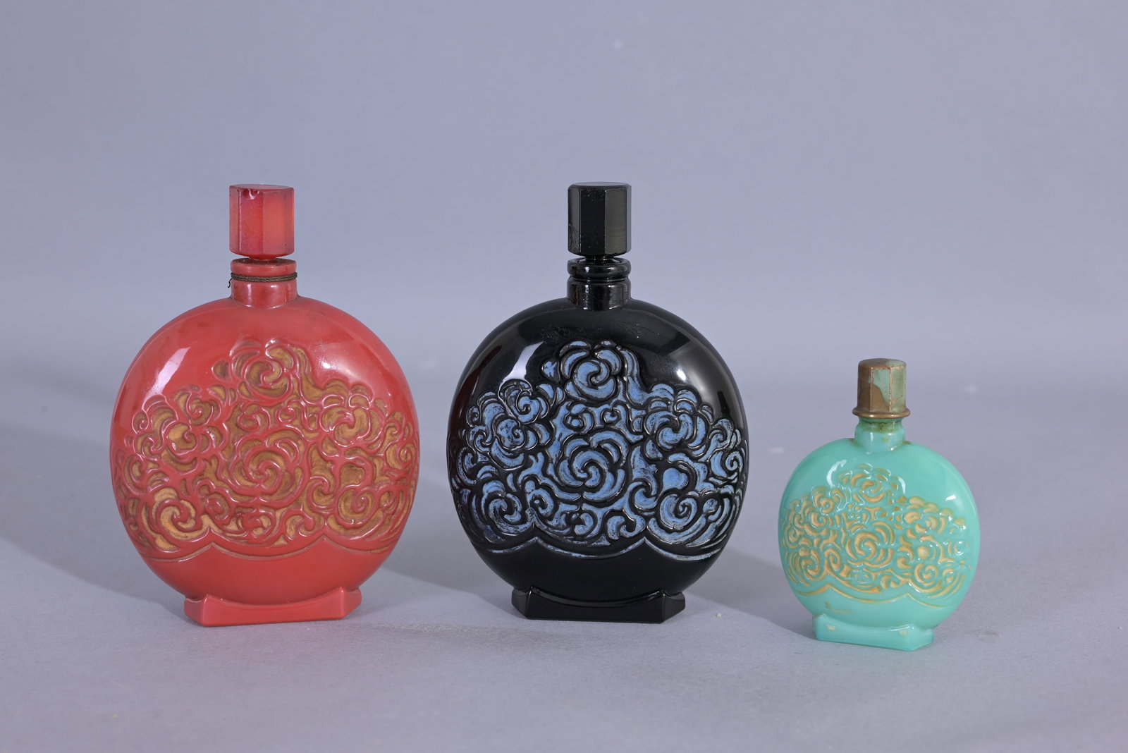 (3) Lionceau Parfum Pour Brunes Perfume Bottles: - Lionceau - Medium red scroll bottle. Parfum Pour Brunes. Circa 1925 - Lionceau - Medium black scroll bottle. Le Fleuve Bleue. Circa 1925 - Lionceau - Small green scroll bottle. (Lionceau - 2,3,4) Pr
