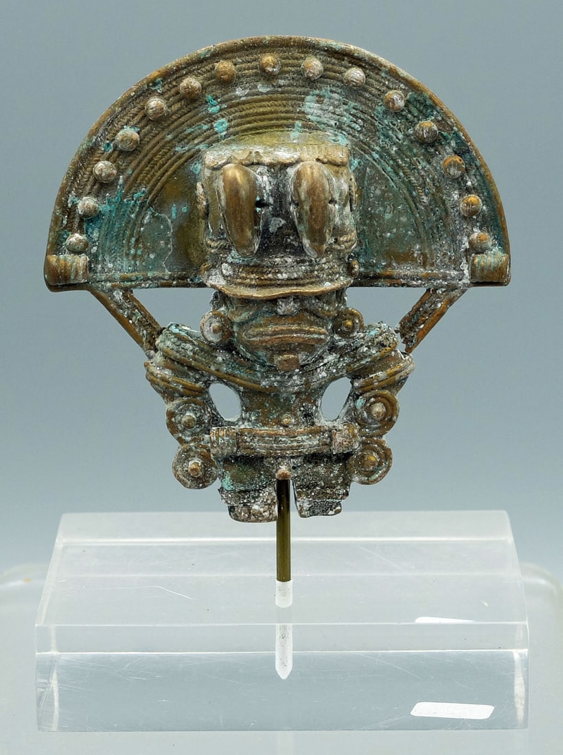 Tairona tumbaga pendant from Colombia: A choice Tairona tumbaga pendant from Colombia, ca. 1000 - 1500 AD. It is 3 in. high and portrays a shaman wearing a fancy ceremonial headdress consisting of two bird heads and a solar symbol. He is l