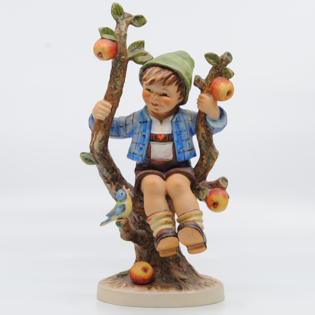 Goebel "Apple Tree Boy" Collector Figurine TMK-5: Goebel "Apple Tree Boy" figurine. Figurine of a little boy wearing a blue jacket and green hat, sitting on an apple tree branch. There is a little bird perched on one of the branches. Imprinted MJ Hum