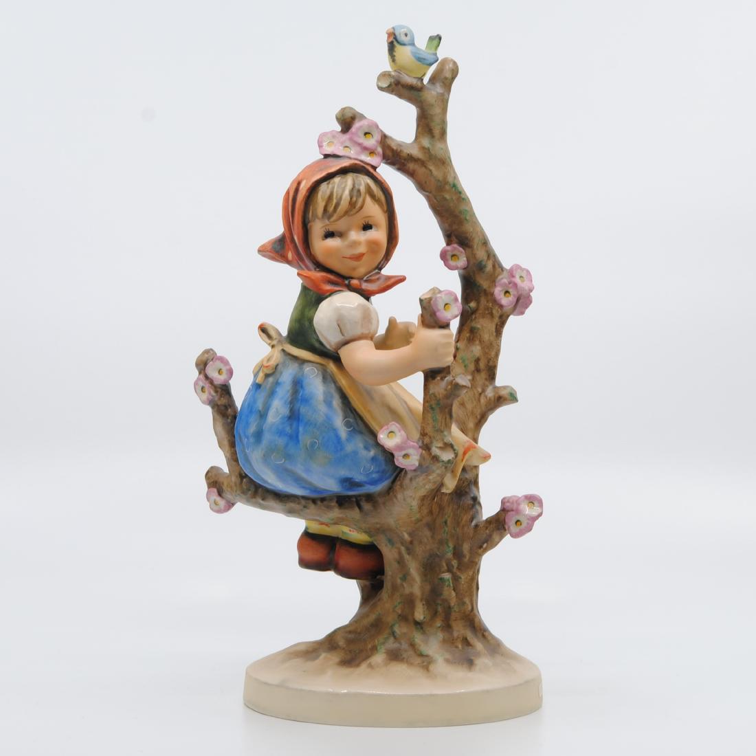 Goebel "Apple Tree Girl" Collector Figurine TMK-6: Goebel "Apple Tree Girl" figurine. Figurine of a little girl in a blue dress with a red head scarf, sitting on an apple tree branch. There is a little bird perched at the top of the tree. Imprinted MJ