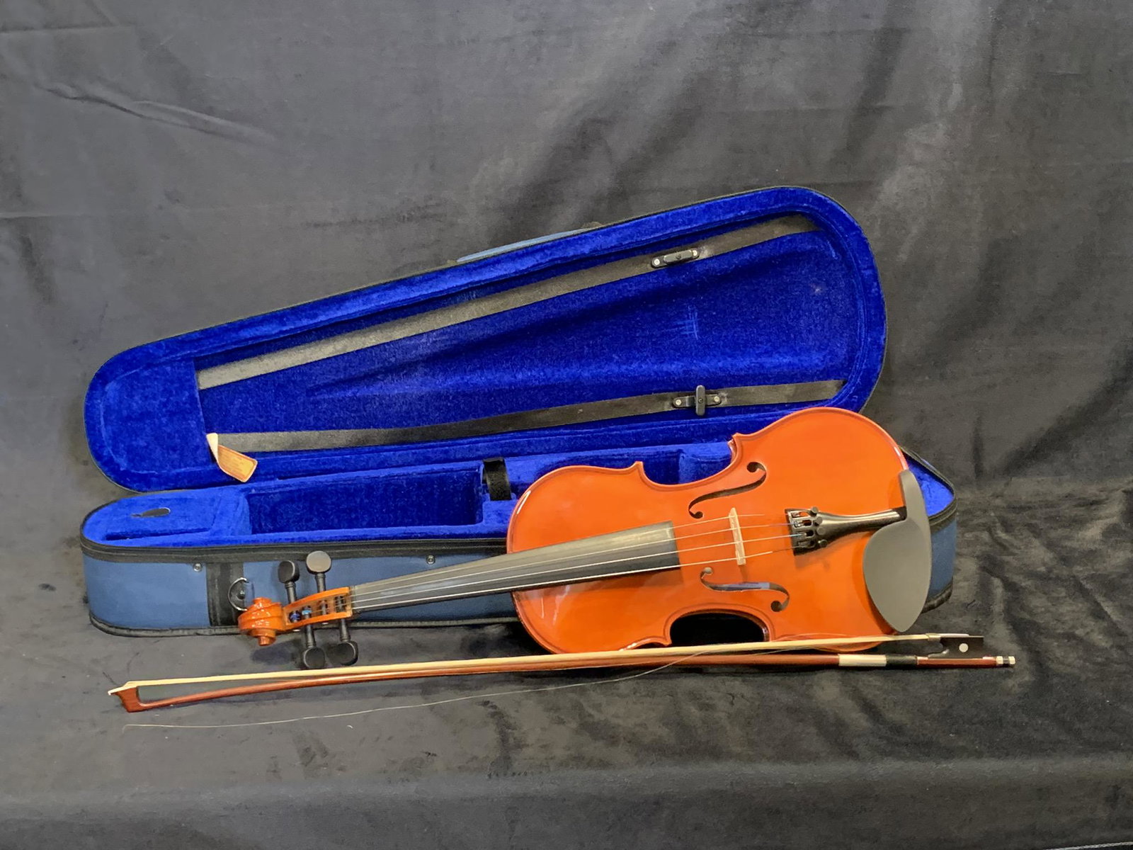 Mezel Violin with Case: A Mezel violin with wooden bow, and blue carrying case. Included as well are straps, and a small container of violin rosin. Violin: 23" x 8" x 3 1/4" thick. Case: 32" x 10" x 6" thick